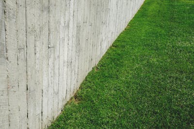 A well cared for rental investment home featuring a wooden fence alongside a lush green lawn.
