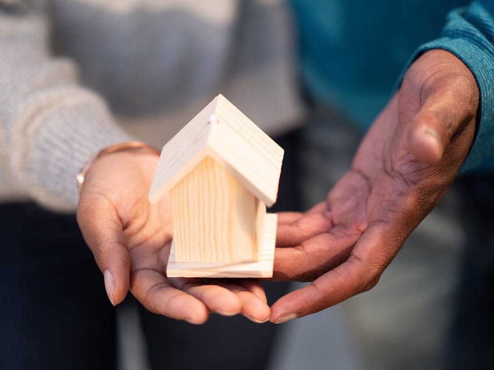 Hands holding a small wooden house model, showing that affordable housing is available in South Carolina.