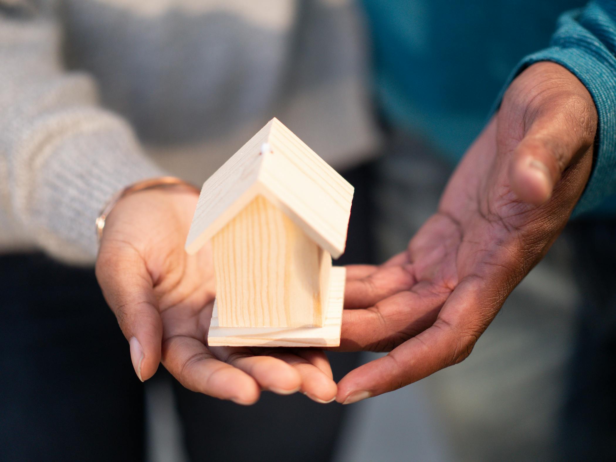 Hands holding a small wooden house model, showing that affordable housing is available in South Carolina.