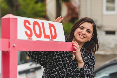 Smiling realtor holding a 'Sold' sign in front of a South Carolina house.