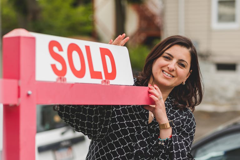 Smiling realtor holding a 'Sold' sign in front of a South Carolina house.