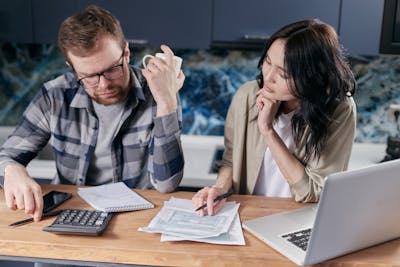 A couple reviews bills and documents on a laptop while discussing household finances showcasing why nearly half of home buyers have regrets.