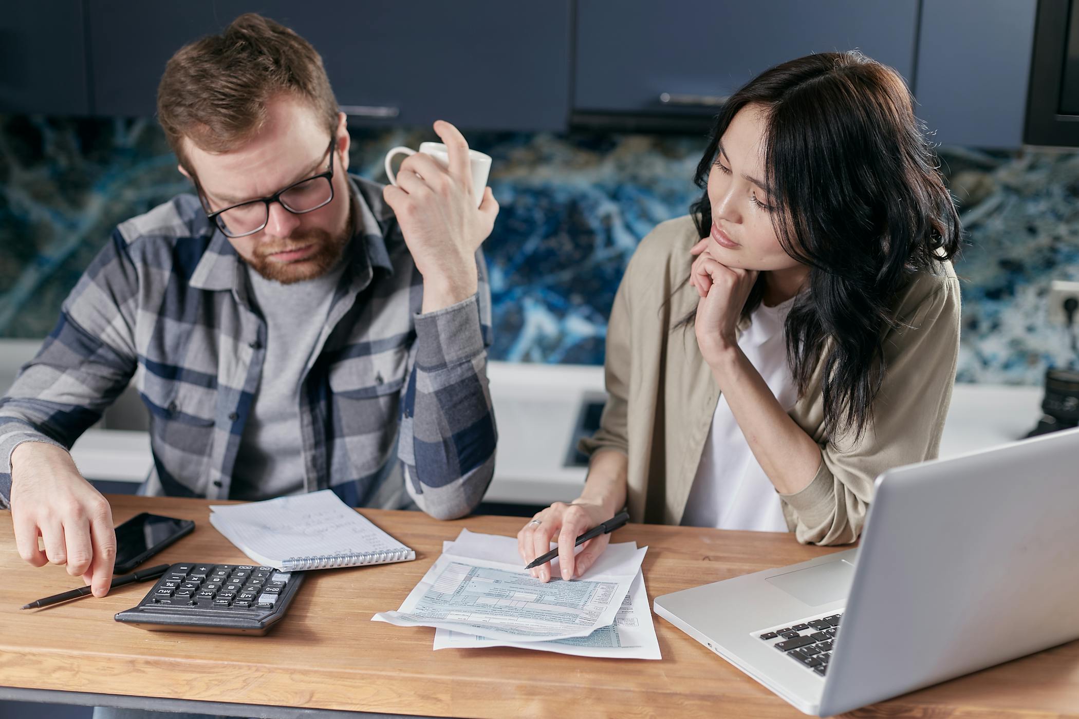A couple reviews bills and documents on a laptop while discussing household finances showcasing why nearly half of home buyers have regrets.