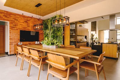 A stylish dining room featuring a wooden table, hanging greenery, and brick wall decor showcasing dining rooms are vanishing from modern homes.