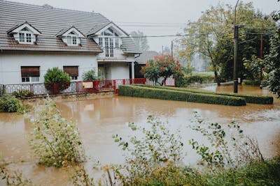 A suburban house surrounded by floodwaters after heavy rain, showing impact of natural disaster and how climate change could trigger home foreclosures.