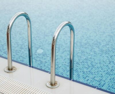 Clear swimming pool with stainless steel handrails and reflections of trees showcasing pools may not be worth the investment in the real estate market.