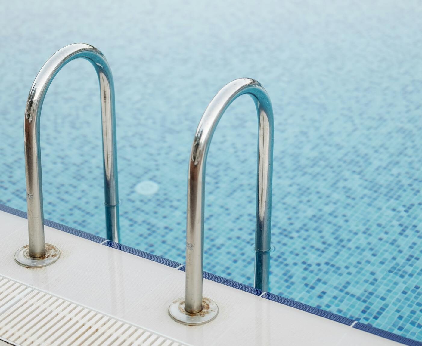 Clear swimming pool with stainless steel handrails and reflections of trees showcasing pools may not be worth the investment in the real estate market.