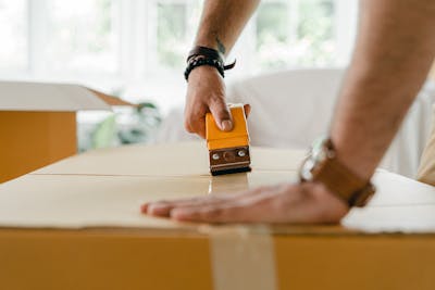 Close-up of a man sealing a cardboard box with a tape dispenser during a move indoors showcasing migration patterns in South Carolina.