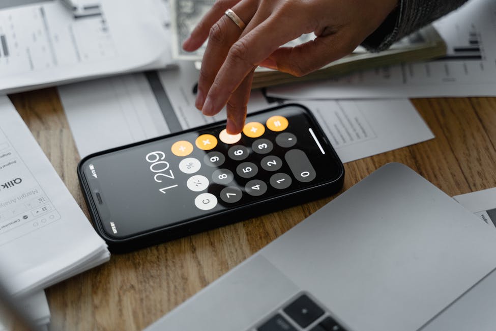 Close-up of a person using a smartphone calculator on a table with documents for financial calculations showcasing the cracking down on rental price manipulation for tenants.