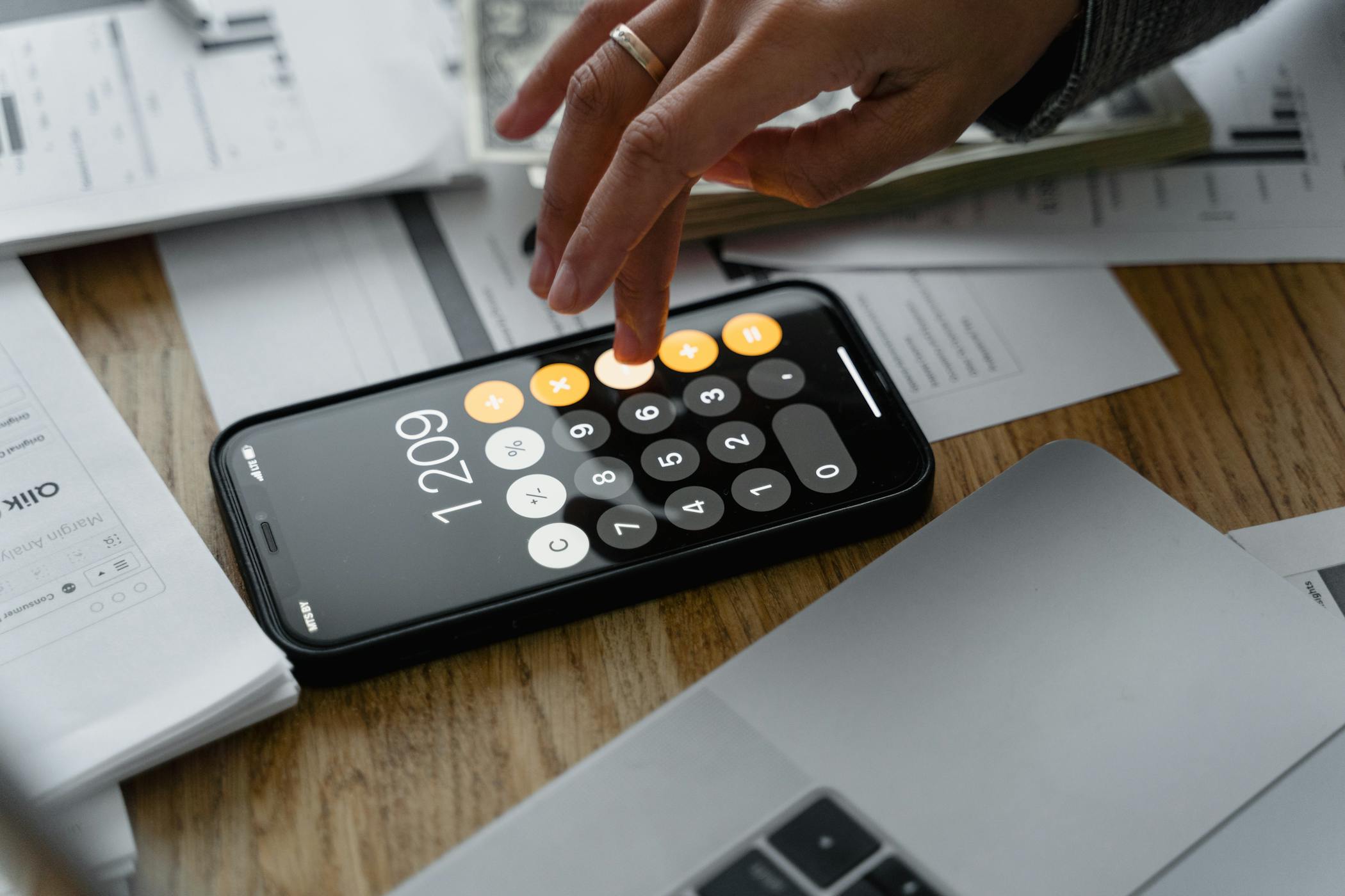 Close-up of a person using a smartphone calculator on a table with documents for financial calculations showcasing the cracking down on rental price manipulation for tenants.