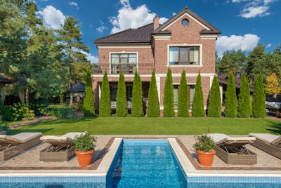 Facade of brick dwell villa with green bushes on lawn and sunbeds near swimming pool showcasing North Carolina residents now able to rent out backyard swimming pools.