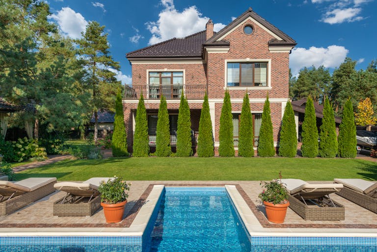Facade of brick dwell villa with green bushes on lawn and sunbeds near swimming pool showcasing North Carolina residents now able to rent out backyard swimming pools.