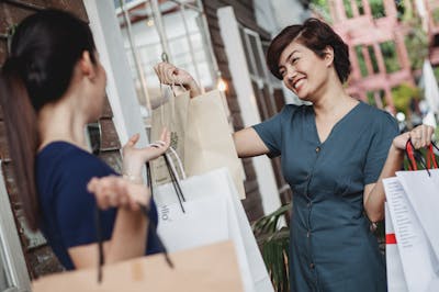 Two women smiling and holding shopping bags outdoors, enjoying a sunny day in Rock Hill, South Carolina.