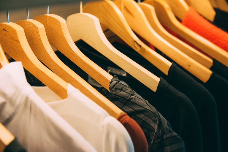 A close-up view of a row of clothes on wooden hangers, showcasing various fabrics and colors in a wardrobe setting demonstrating Gildan buying out Hanesbrands in Winston Salem, NC.