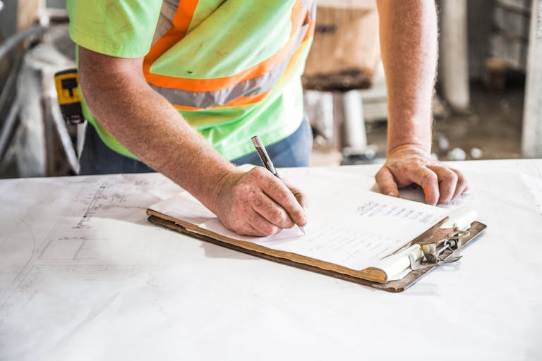 A construction worker writes notes on a clipboard at a construction site, emphasizing planning and precision showcasing Greenville County placing a temporary moratorium on a certain type of residential construction.