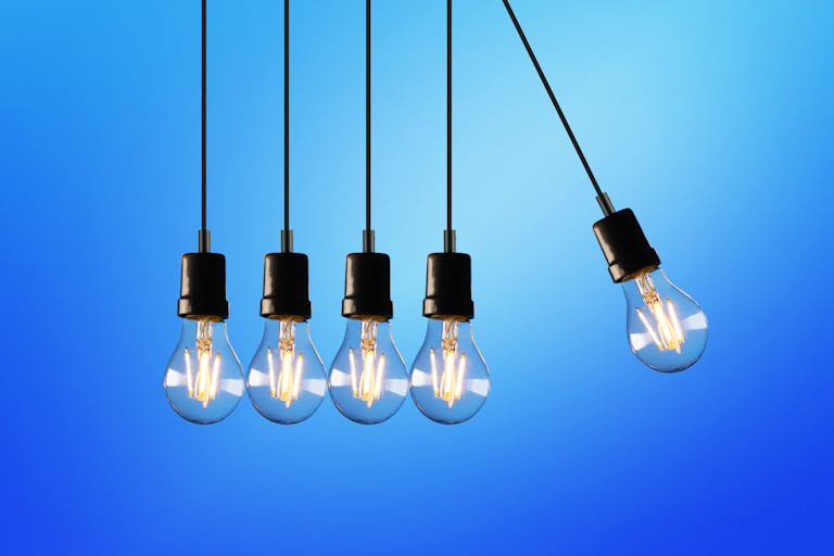 Hanging Edison-style light bulbs against a vibrant blue backdrop, showcasing the soaring electricity costs and how they are reshaping the rental market.