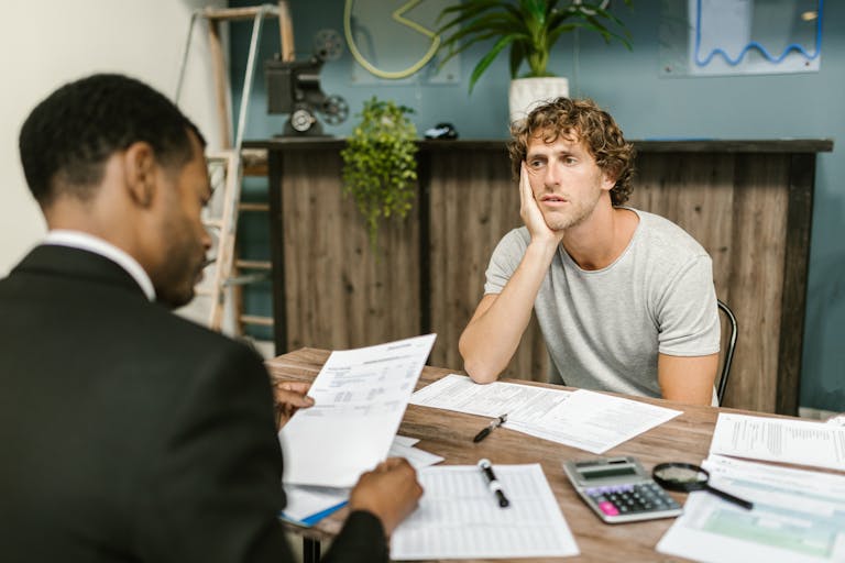 Man in office, appearing stressed during paperwork discussion, sitting opposite professional showcasing the rise in foreclosures across America.