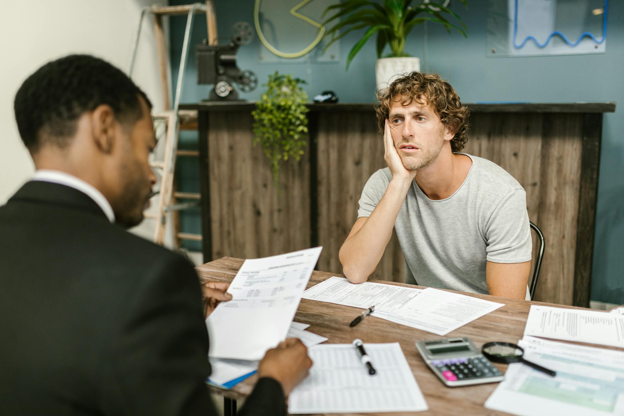 Man in office, appearing stressed during paperwork discussion, sitting opposite professional showcasing the rise in foreclosures across America.