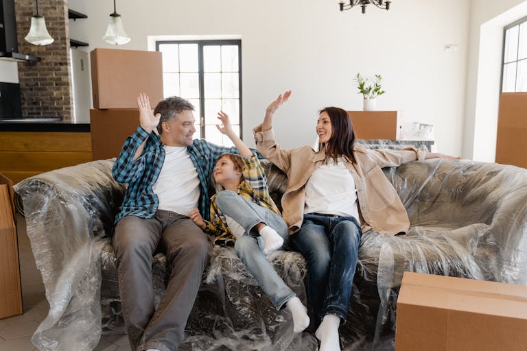 A cheerful family sitting on a couch amidst moving boxes, celebrating their rental home and how rent growth has slowed to its lowest point.