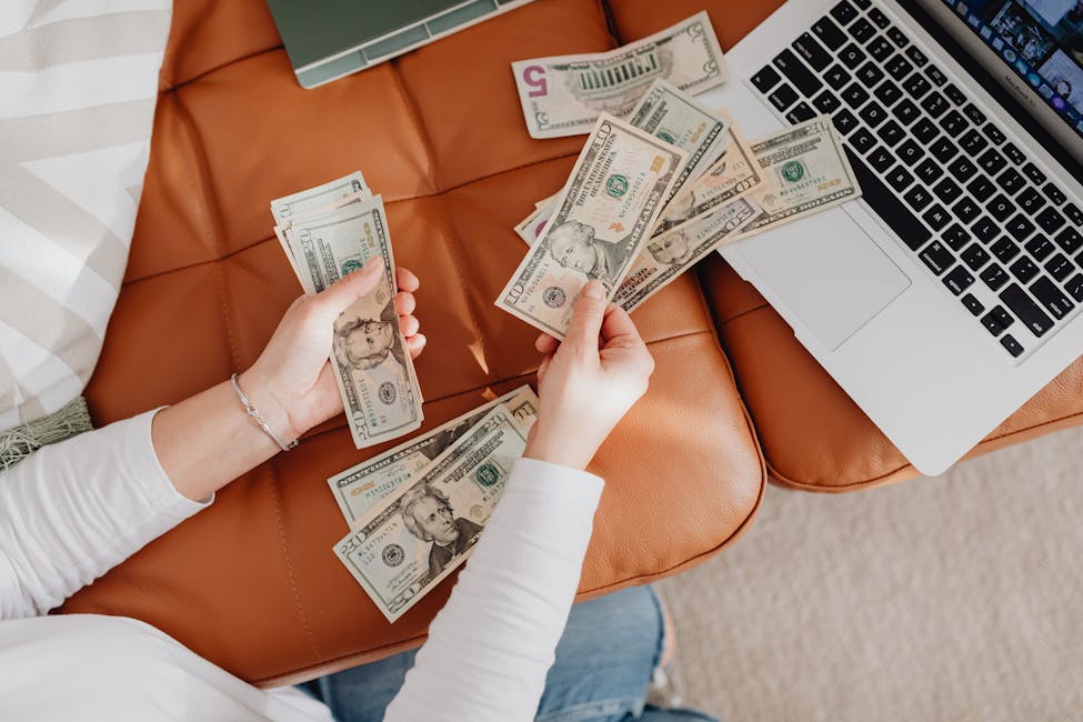 A person counts US dollar bills on a couch with a laptop, symbolizing a tenant paying their monthly rent payment.