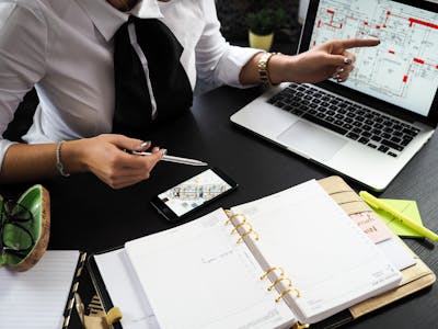 A business professional working on real estate project plans using multiple devices in an office setting showcasing a possible upcoming real estate boom.