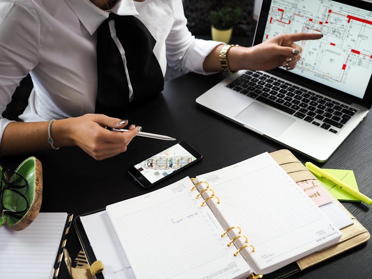 A business professional working on real estate project plans using multiple devices in an office setting showcasing a possible upcoming real estate boom.