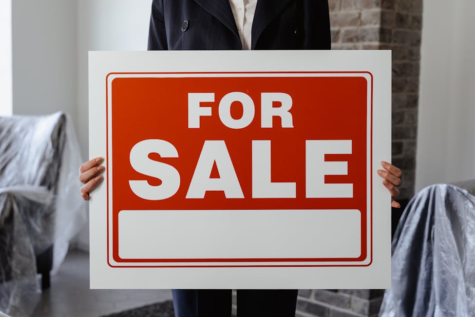 Close-up of a person in a suit holding a For Sale sign in a furnished room showcasing America's lowest home-moving rate in nearly 30 years.