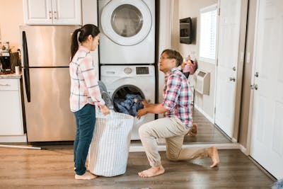 Couple managing household chores by throwing laundry in a washing machine that is provided by the owners of the rental property.