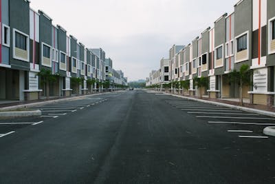 A quiet, empty urban street flanked by modern condominiums under a cloudy sky.