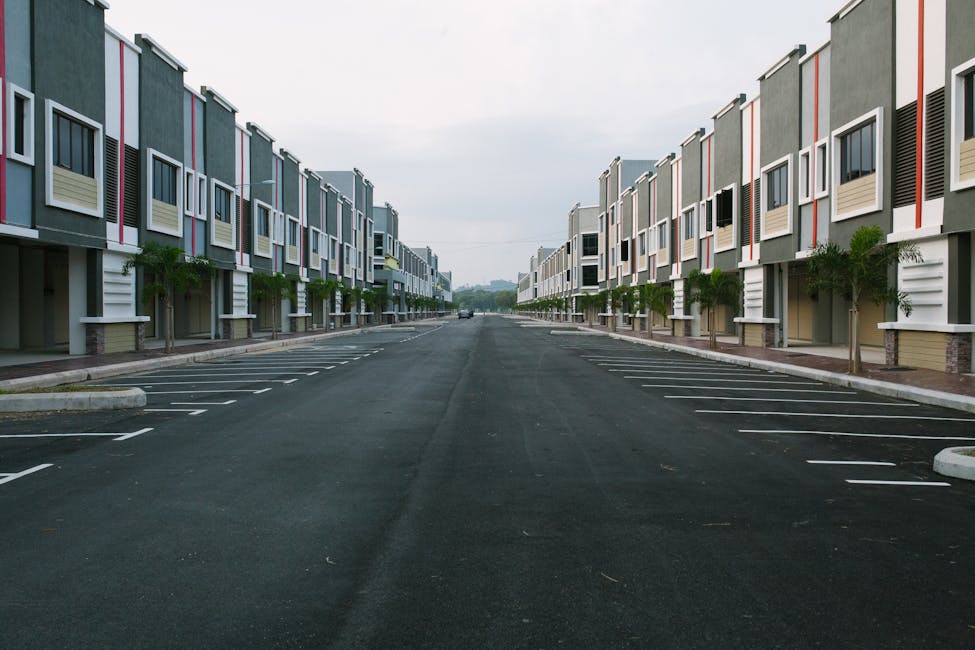 A quiet, empty urban street flanked by modern condominiums under a cloudy sky.