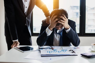 An overwhelmed businessman grasps his head, surrounded by reports in a bright office showcasing Charlotte making job cuts due to AI.