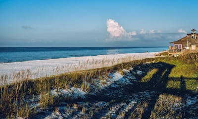 Scenic beach view with a house, blue skies, and ocean waves on a sunny day showcasing the #1 place Americans want to move to, Brunswick County, NC.