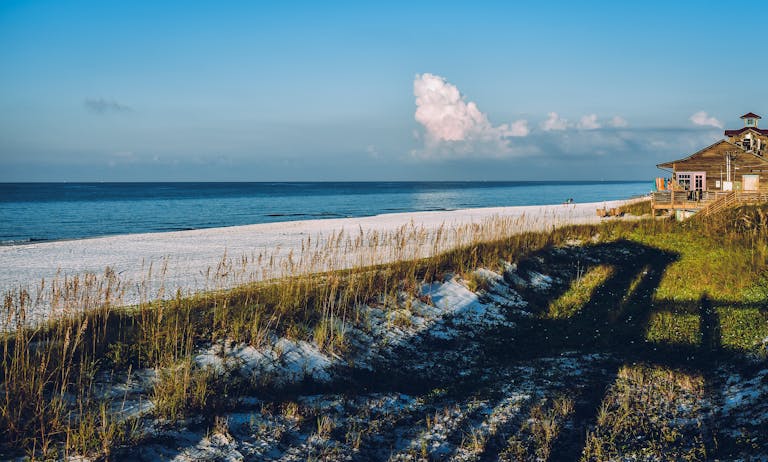 Scenic beach view with a house, blue skies, and ocean waves on a sunny day showcasing the #1 place Americans want to move to, Brunswick County, NC.